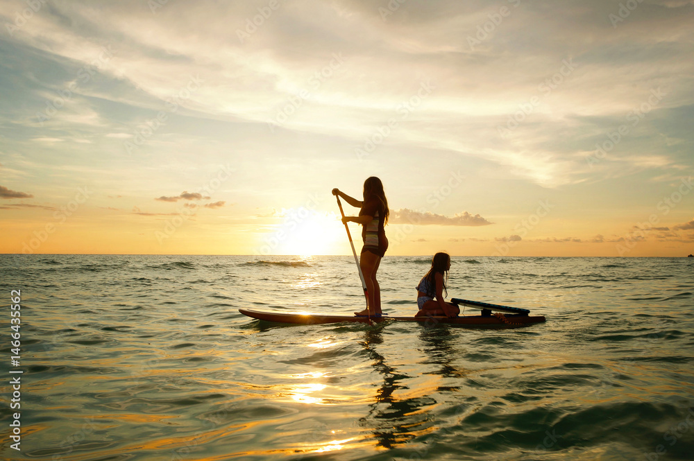Profile teen sisters paddleboarding in Gulf of Mexico at sunset Profile teen sisters paddleboarding in Gulf of Mexico at sunset
