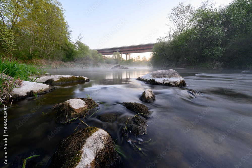 Sunrise over a misty river surrounded by lush green trees in spring. Tranquil nature landscape with calm water, fog, and golden sunlight reflecting on the surface. Ideal for eco, travel, wellness.