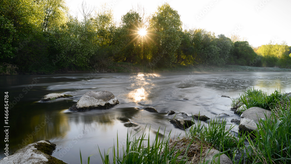 Sunrise over a misty river surrounded by lush green trees in spring. Tranquil nature landscape with calm water, fog, and golden sunlight reflecting on the surface. Ideal for eco, travel, wellness.