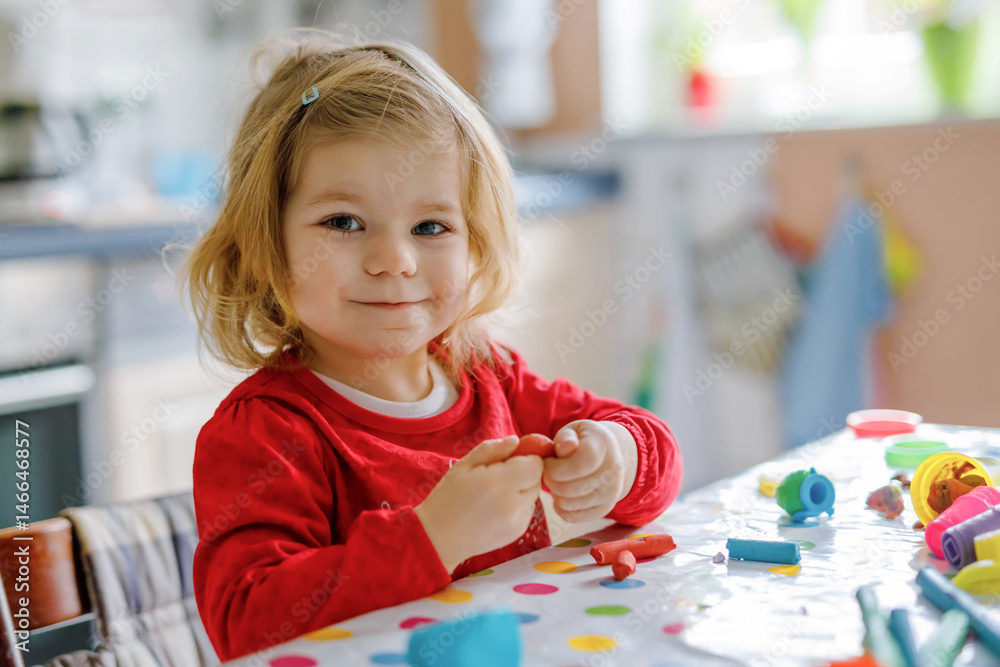 Fototapeta premium Adorable cute little toddler girl with colorful clay. Healthy baby playing and creating toys from play dough. Small kid molding modeling clay and learning
