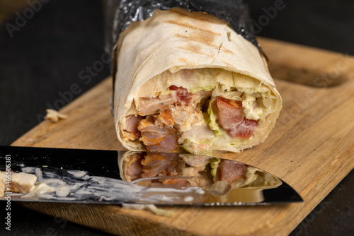 shawarma from thin tortilla with meat , fast food made from various ingredients packed in foil, close up