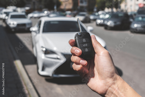 Close-up of a woman unlocking a car using a key fob, with a white car parked in a car park in the background.