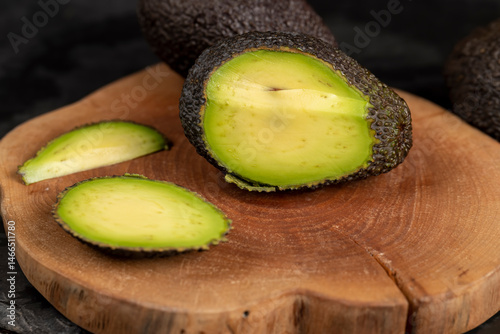 cut avocado with green flesh on a wooden cherry board, sliced small avocado with soft overripe flesh on a wooden board