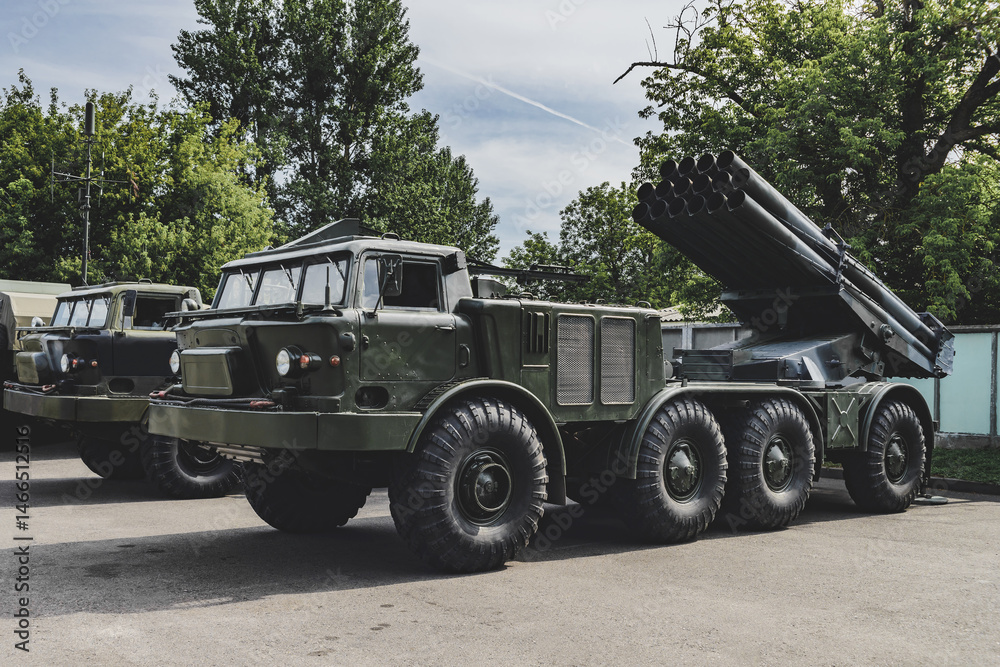 Obraz premium Military vehicle Rocket artillery with camouflage coloring stands in a car park. Background of nature and trees.