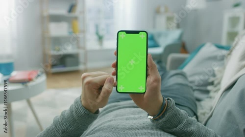 Man holding smartphone vertically, lying on sofa while making video call at home