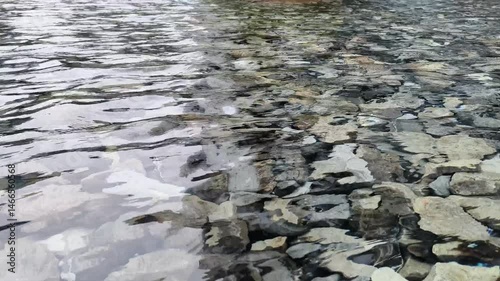 Pebblestones are under a crystal-clear surface, and water ripples