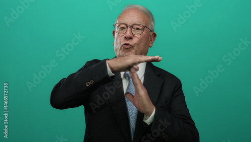 Senior man in a business suit makes a timeout gesture against a vibrant green background, conveying a need for pause or interruption in a professional setting.