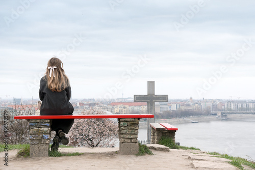 Young woman sitting alone on a bench against city view