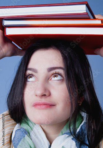 Obraz na płótnie Portrait of female student balancing books on her head as symbol of education, knowledge and self development. Vertical image. w salonie