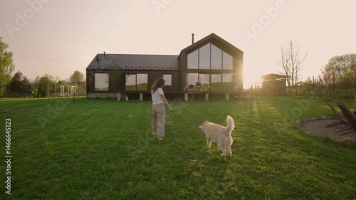 woman playing with her siberian husky dog outside modern barnhouse on a freshly mowed lawn in the countryside during sunset