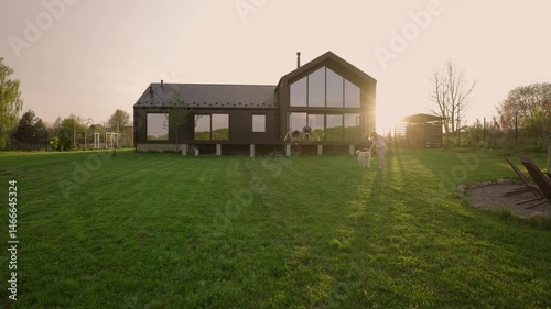 woman playing with her siberian husky dog outside modern barnhouse on a freshly mowed lawn in the countryside during sunset