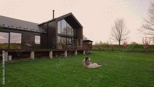 woman playing with her siberian husky dog outside modern barnhouse on a freshly mowed lawn in the countryside during sunset