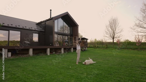 woman playing with her siberian husky dog outside modern barnhouse on a freshly mowed lawn in the countryside during sunset