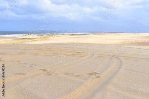 A big bright yellow sand dune on the background of bright cloudy sky. Something like a hieroglyph on the surface. Stockton Sand Dunes near the coast, Worimi Regional Park, Anna Bay, Australia. 