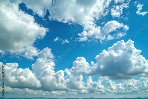 Fototapeta Naklejka Na Ścianę i Meble -  Fluffy white clouds scattered across a bright blue sky above distant mountains during daytime