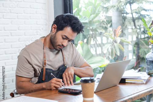 Attractive barista male or employee concentrate on stacks of tax declaration bills, restaurant owner using laptop for bookkeeping control payment, multitask small business lifestyle doing everything