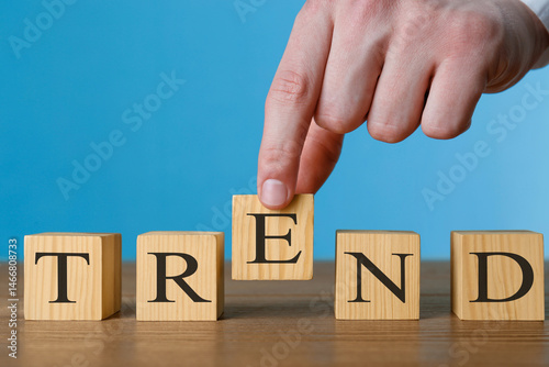 Man making word Trend with wooden cubes at table against blue background, closeup
