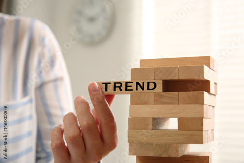 Woman removing wooden block with word Trend from tower indoors, closeup