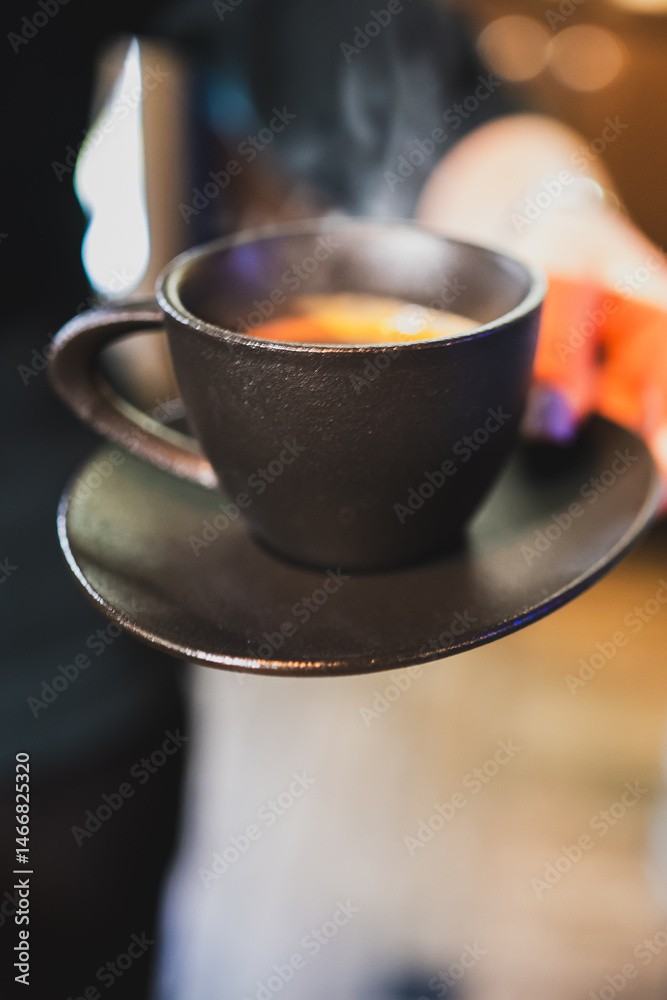 A black ceramic cup with a hot beverage sits on a matching saucer, emitting steam. The cozy atmosphere suggests warmth and freshness, ideal for morning coffee or tea moments.