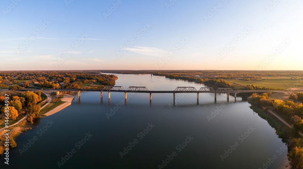 Fototapeta premium A panoramic aerial capture of a bridge spanning a calm river, the geometric lines of its structure contrasting beautifully with the natural curves of the water. 