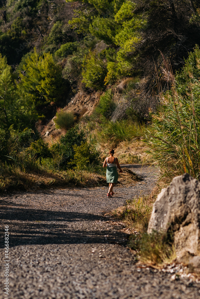 Brunette woman walking on country road between rocks and vegetation.