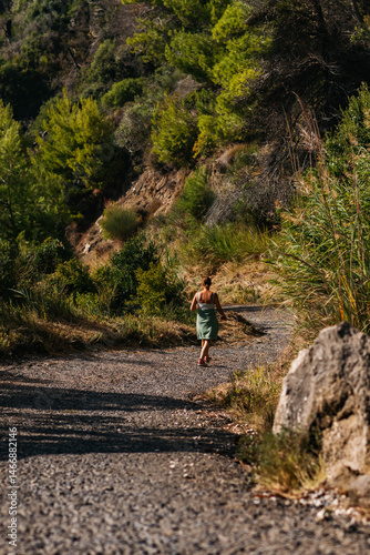 Obraz na płótnie Brunette woman walking on country road between rocks and vegetation. w salonie
