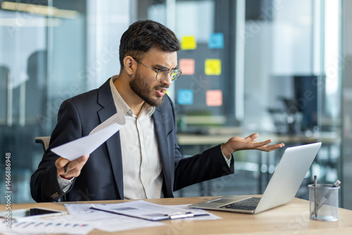Photos A frustrated businessman is looking at his laptop screen in the office, holding