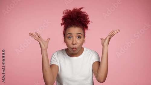 Portrait shocked African American redhead curly woman showing mind explosion gesture, mind blown of ideas looking camera. Female in white t-shirt standing on isolated pink background with copy space