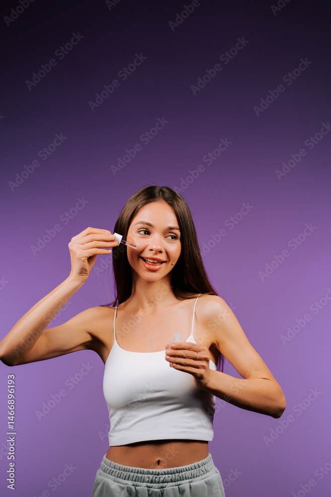 Woman applying face serum with a pipette in a vibrant purple backdrop Woman applying face serum with a pipette in a vibrant purple backdrop
