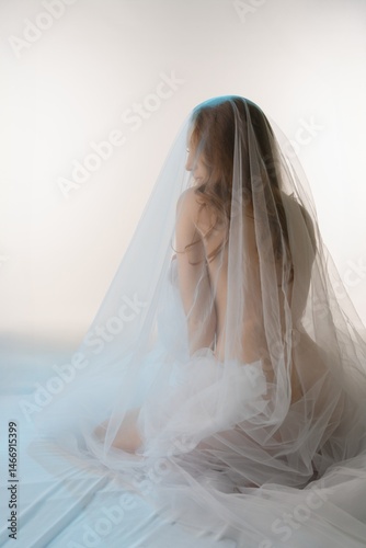 Sensual beauty draped in delicate fabric poses in a serene setting