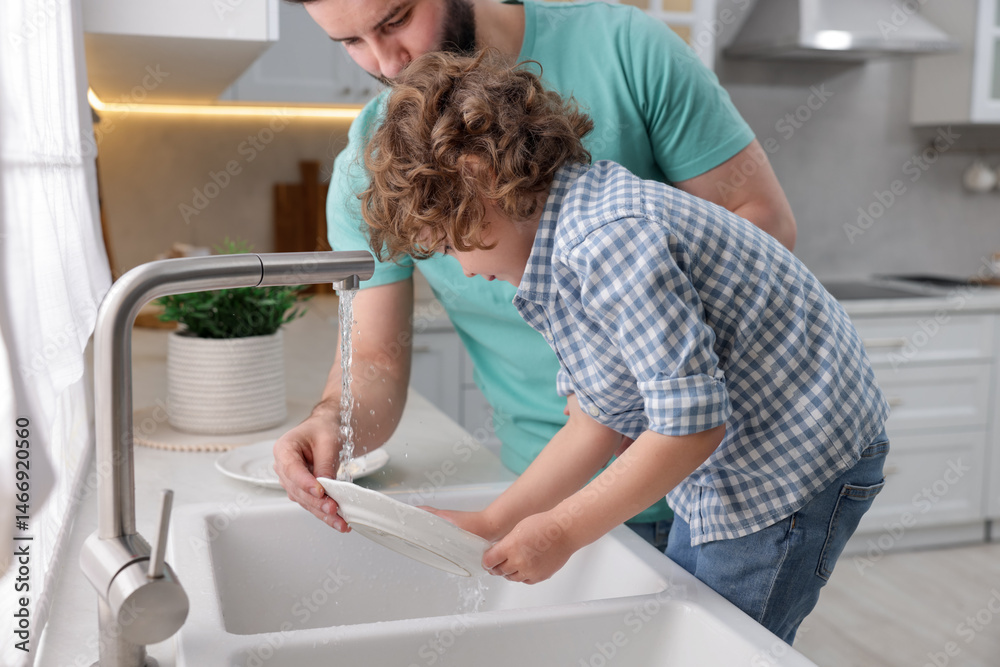 Fototapeta premium Father and his son washing dishes together in kitchen at home