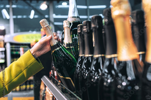 Hand selecting champagne bottle from shelf in store.