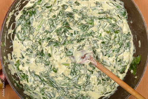 Obraz na płótnie A top-down view shows creamy spinach being stirred in a dark pan with a wooden spoon w salonie
