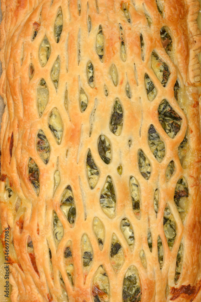 An overhead shot shows a baked puff pastry pie filled with spinach and cheese on parchment paper
