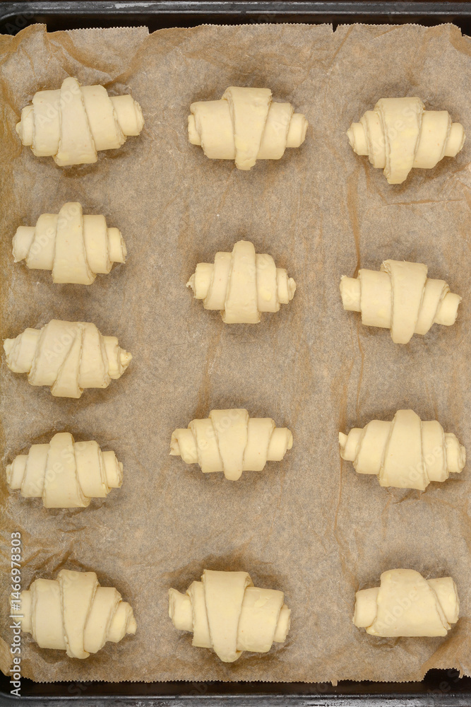 An overhead close-up of raw, rolled croissant dough pieces arranged on parchment paper before baking