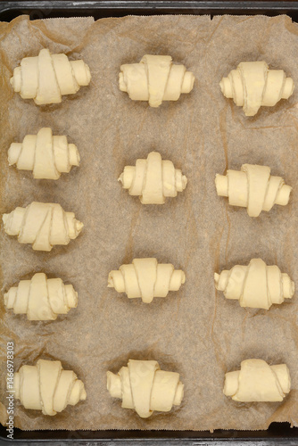 Obraz na płótnie An overhead close-up of raw, rolled croissant dough pieces arranged on parchment paper before baking w salonie