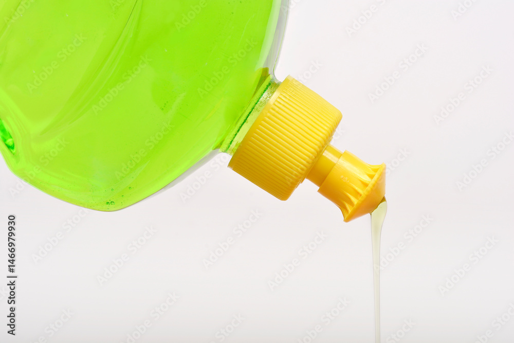Tilted clear plastic bottle with a yellow cap pours a stream of light green dish soap