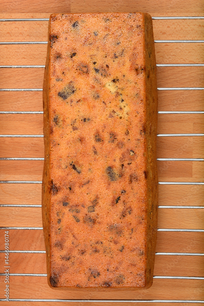 A baked loaf cake with walnuts, raisins, chocolate pieces, and orange zest cooling on a wire rack over a wooden surface