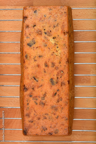A baked loaf cake with walnuts, raisins, chocolate pieces, and orange zest cooling on a wire rack over a wooden surface