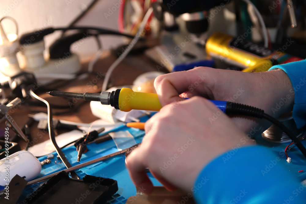 Close-up of a hand soldering a phone circuit board with a yellow soldering iron and copper bit. Repair master at work