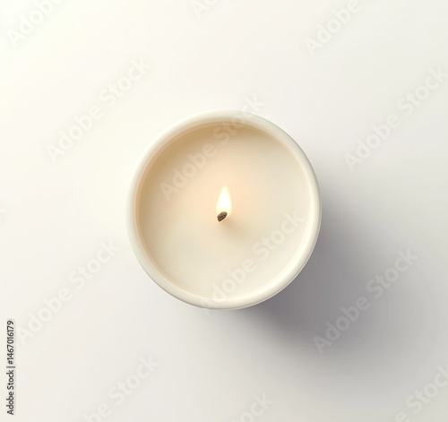 Single round candle, cream colored, lit.  Small, round,  wax candle with a lit wick.  Top view against white background.  Simple, elegant, and understated design