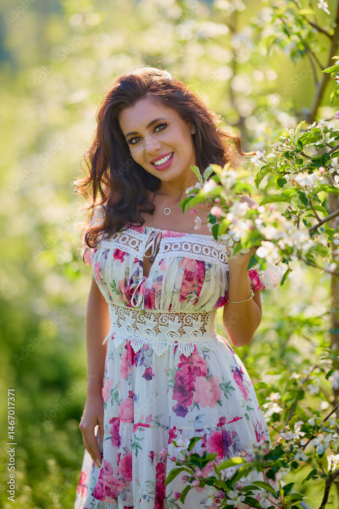 portrait of a beautiful woman in a dress in a blooming apple orchard enjoying a sunny spring day
