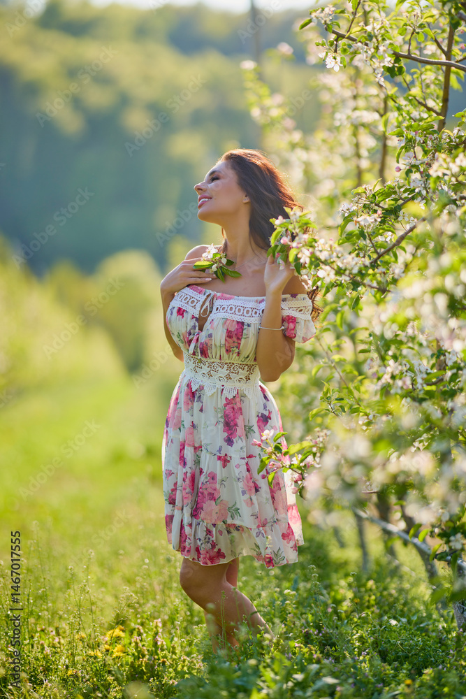Full body portrait of a beautiful woman in a dress in a blooming apple orchard on a sunny spring day