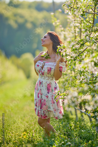 Obraz na płótnie Full body portrait of a beautiful woman in a dress in a blooming apple orchard on a sunny spring day w salonie