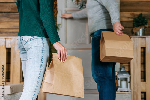 Close-up of a paper bag in a woman's hand against the background of a man with craft packaging indoors.