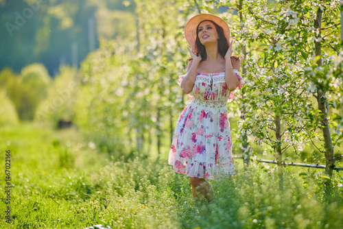 Full body portrait of a beautiful woman in a dress in a blooming apple orchard on a sunny spring day