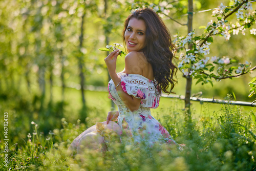 Obraz na płótnie portrait of a beautiful woman in a dress in a blooming apple orchard enjoying a sunny spring day w salonie
