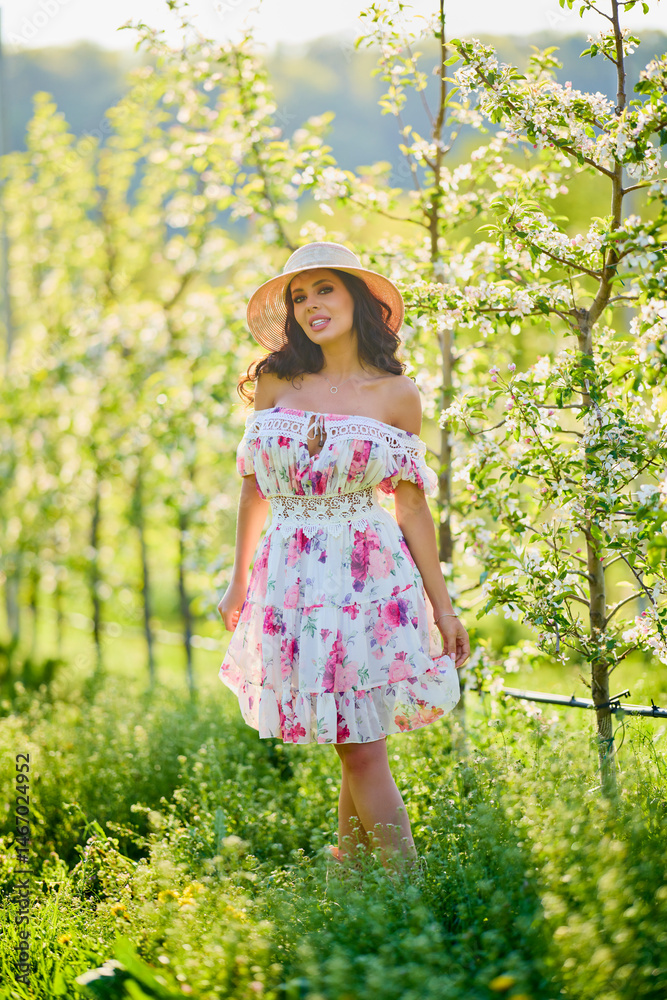 Full body portrait of a beautiful woman in a dress in a blooming apple orchard on a sunny spring day