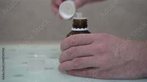 unscrewing the medicine cap, Pouring Medicine Into Measuring Cup, man Hands Pour Medical Syrup Into Measuring Plastic Cup