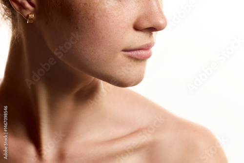 Konstfotografi Side view portrait of young woman, focusing on her jawline, neck, and shoulder, showcasing natural skin with freckles against white background